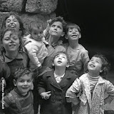 BAMBINI vivaci, in posa nel vicolo guardano tutti all'insù, tranne i più curiosi che guardano divertiti il fotografo. Hanno tutti espressioni allegre e scherzose. Fotografia di Ando Gilardi da ampio servizio, Palermo, cortile Scalilla 1957.